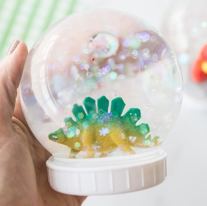 A dinosaur toy in an upside down jar filled with water and glitter.