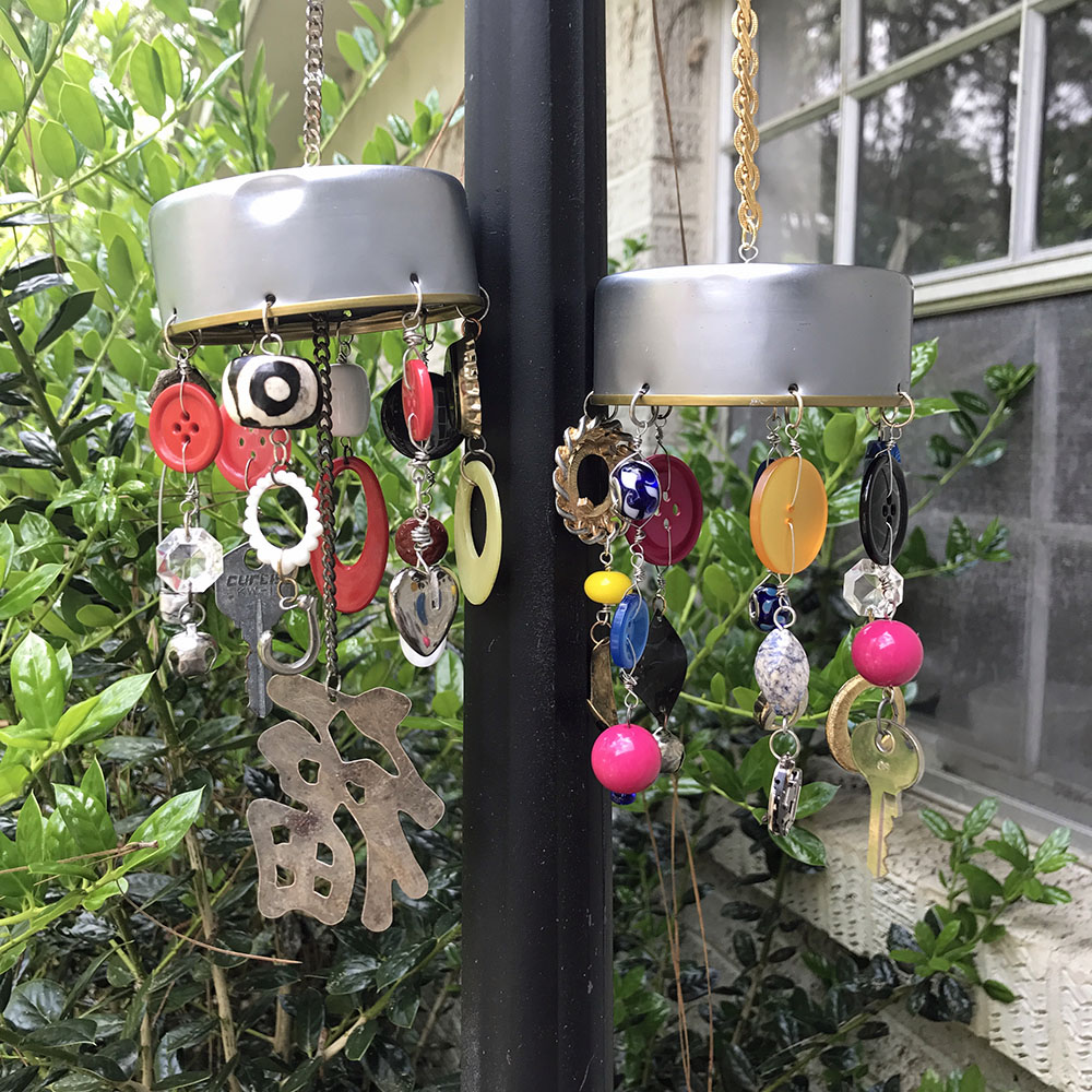 A photograph featuring wind chimes made out of a tuna can and miscellaneous items like buttons, chains, keys, beads, etc. 