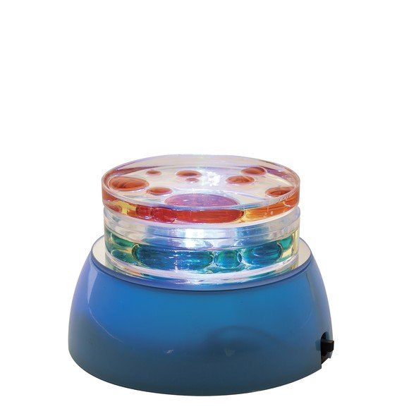 A round flat light sorce with a jar of liquid on top that has multi colored blobs in it.