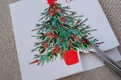 Scissors cutting a picture of a Christmas tree from a card