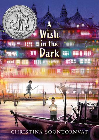 The cover of "A Wish in the Dark" by Christina Soontornvat, featuring an illustration of two children with a luminescent building in the background.