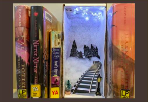 A photograph of a bookshelf diorama with cotton, train tracks, cutouts, and lights placed between young adult books.