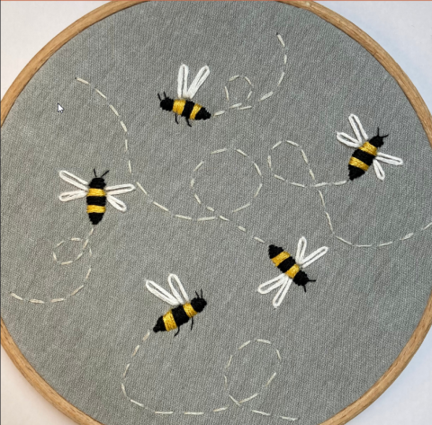 An embroidery hoop with five small bees stitched onto gray fabric.