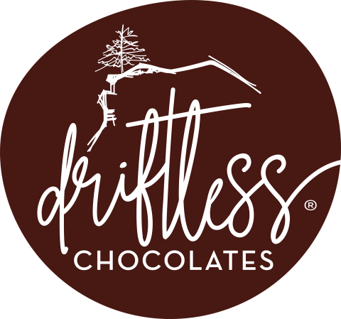 Driftless Chocolates logo. Flowing white text in a chocolate brown circle. A white line drawing of a pine tree on a bluff at top.