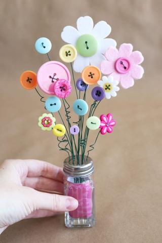 A salt shaker with green wire stems sticking out with buttons shaped like flowers at the end.