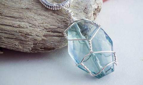A photograph of a blue crystal wrapped in silver wire. 