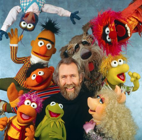 Jim Henson smiling while surrounded by Muppets like Kermit, Miss Piggy, Bert, Ernie, and more.