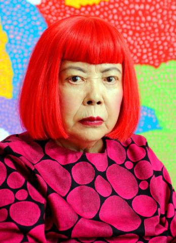 Photo of the artist Yayoi Kusama with bright red hair and a brightly colored background.