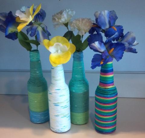 A photograph of four yarn wrapped bottles, each holding flowers.