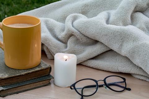 photo of cozy blanket, candle, coffee and reading glasses in muted colors