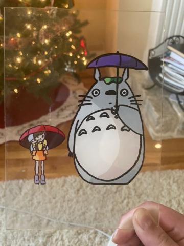 Picture of a large wooly creature holding an umbrella, next to two young girl also holding an umbrella. The image is painted on glass. 