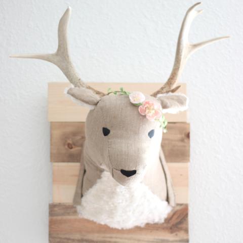 A photograph of a stuffed deer head with flowers mounted on a wooden board.