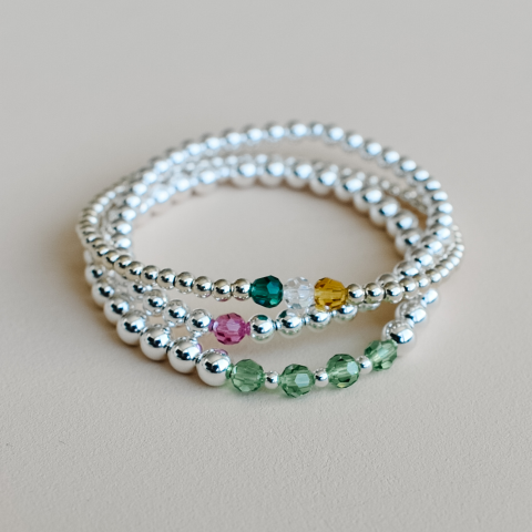 Three mostly silver beaded bracelets with colored crystals in the front.