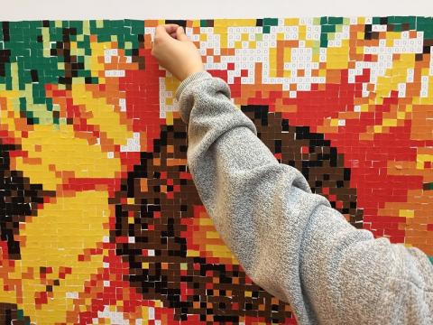 Photo of a hand placing a sticker on a sunflower sticker mosaic. 