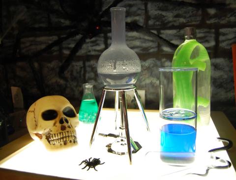 A skull and various jars on a glowing white table in a dark stone room.