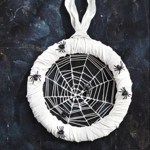 A round white wreath with white yarn making a web with spiders on it.