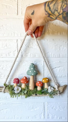 A hand holding a little mushroom wreath with small, colorful mushrooms.