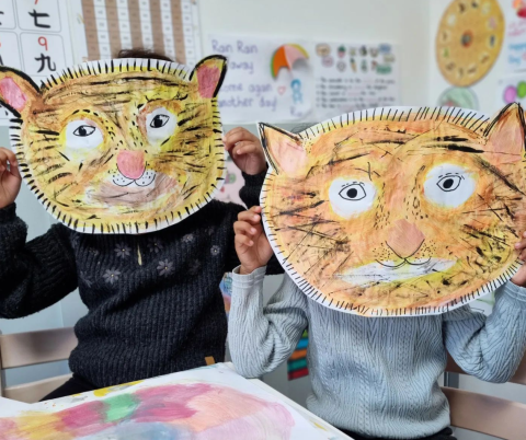 Two children holding painted tiger faces over their own faces. Photo credit to: nikkiandthelittles on Instagram.