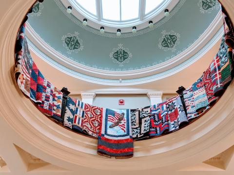 Quilts of Valor. Photo shows the Carnegie-Stout rotunda, with colorful, patriotic quilts of valor draped over the railing.