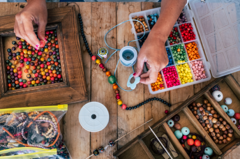 Photo shows a person making a beaded necklace, surrounded by earthy, colorful beads and findings.