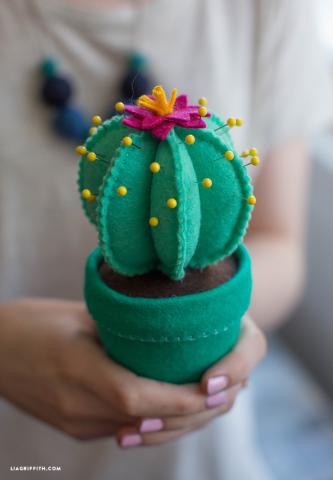 Photo of two hands holding a cactus pincushion made out of green felt.