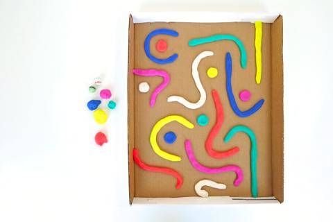 Photo of a cardboard tray with a playdough marble maze set up.