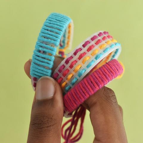Closeup of a hand holding three woven bracelets in blue, pink, and yellow. Image is from HandmadeCharlotte.com