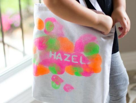 A child holding a book bag with paint splotches.