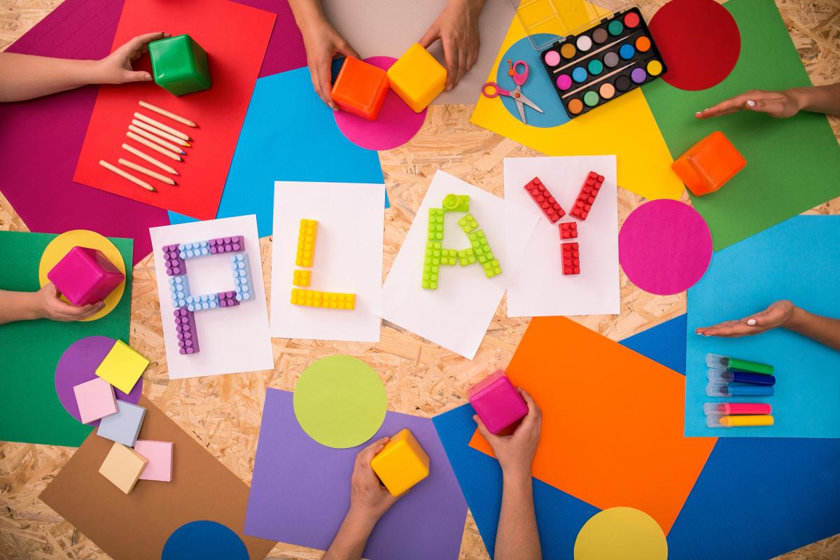 The word "PLAY" made up of LEGO bricks and surrounded by paper, art supplies, etc.