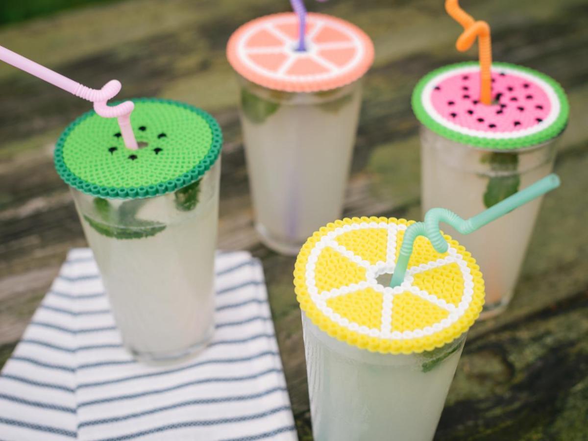 A photograph of four refreshing beverages, each topped with a different perler bead drink cover of different citrus fruits.