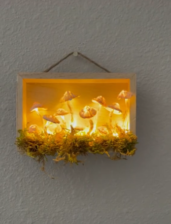 A photograph of glowing mushrooms on top of moss within a wooden frame, hanging on a wall.