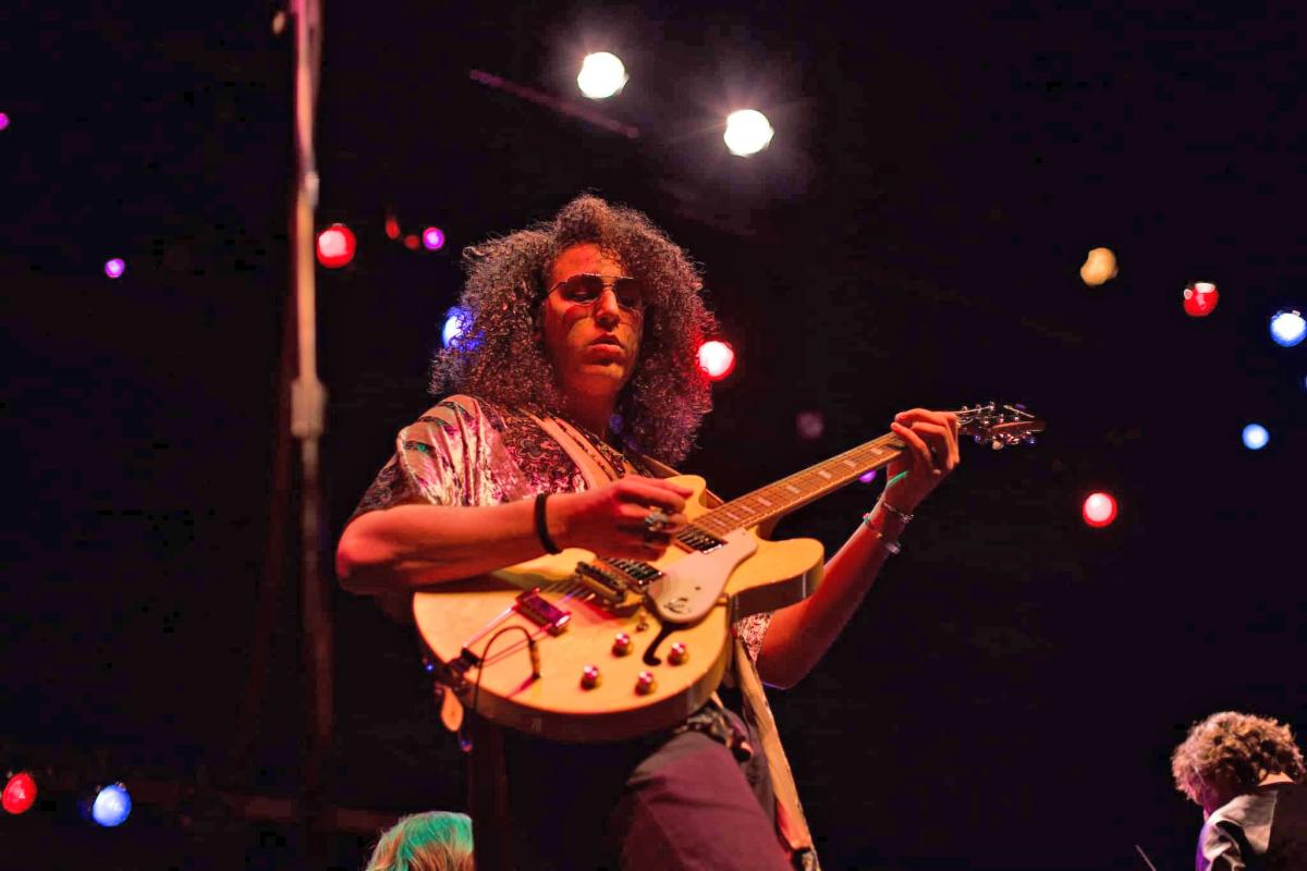 Image of performer Ty Bailey playing guitar in stage lighting. 