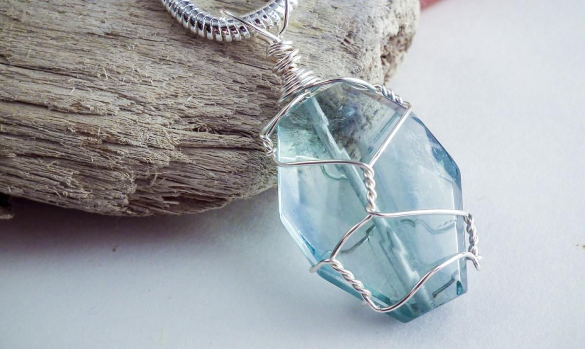 A photograph of a blue crystal wrapped in silver wire. 