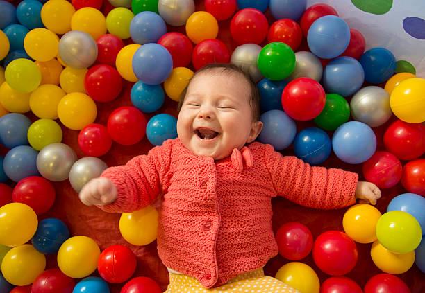 Photo of a laughing baby lying in a ball pit.