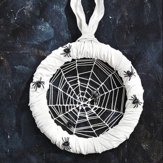 A round white wreath with white yarn making a web with spiders on it.