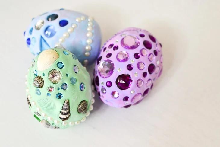 Three eggs with jewels, rocks, and pearls on them. 