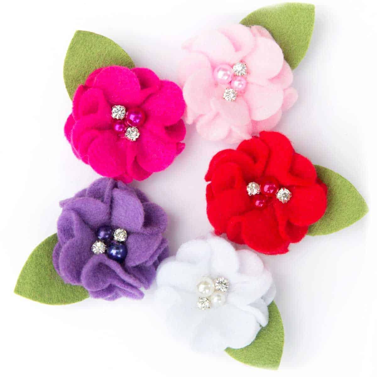 5 flowers made out of felt with beads in the middle and on one larger felt leaf.