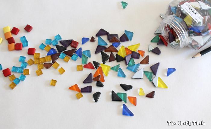 Photo of a jar of colorful mosaic tiles spilled out across a white surface.