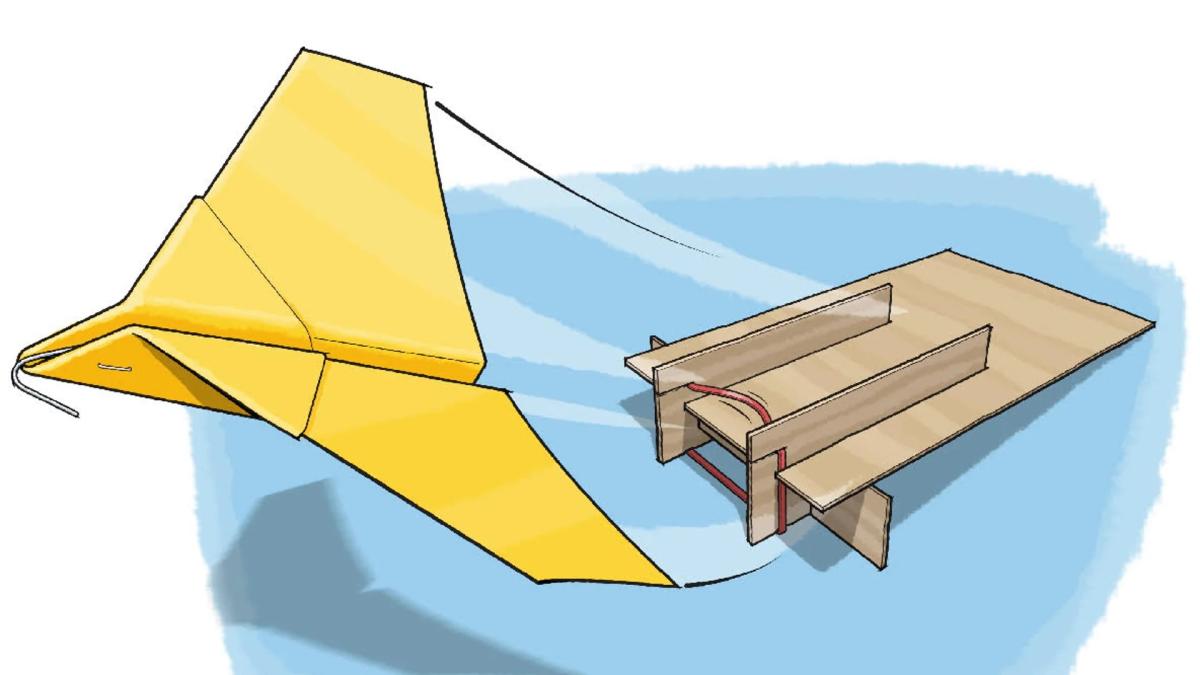 A paper plane being launched from a cardboard ramp with a rubber band. 